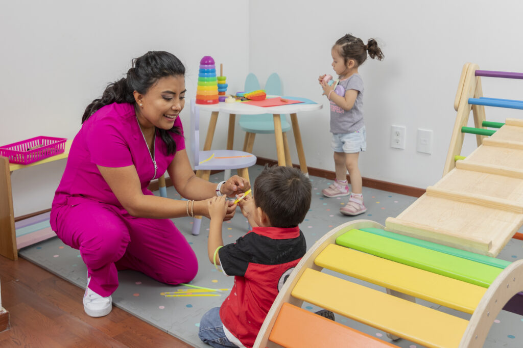 latin pediatrician playing with a child in her medical office, while a girl plays on a table in the background