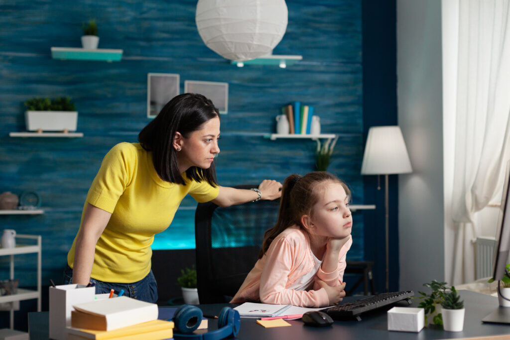 adult mother watching little girl doing schoolwork