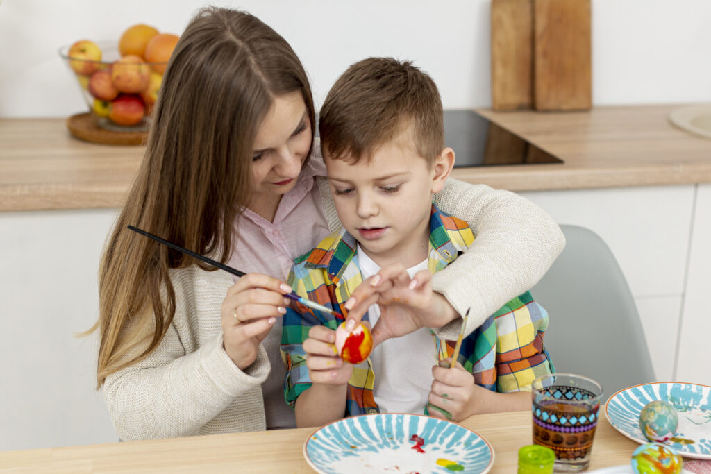 Current image: high angle mom helping son paint eggs
