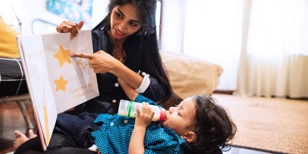 indian woman reads book child woman points book indian family mom child cozy reading time with book bottle indian mom reading book child cozy living room